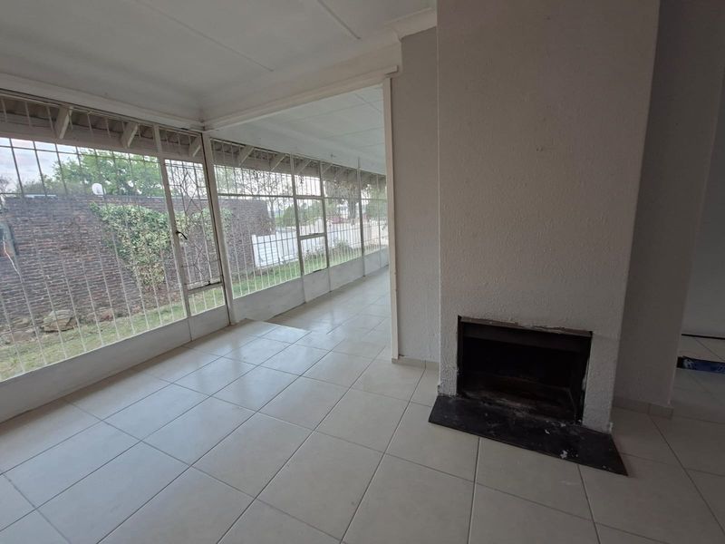 An empty living room featuring tiled flooring, a built-in fireplace, and large windows with security bars overlooking the garden area.