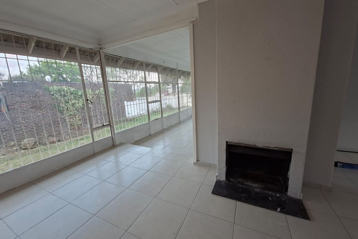 An empty living room featuring tiled flooring, a built-in fireplace, and large windows with security bars overlooking the garden area.