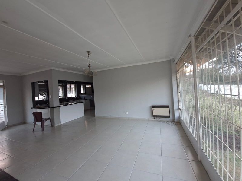 Spacious open-plan living area featuring tiled flooring, a built-in breakfast bar, and large sliding glass doors with security bars.
