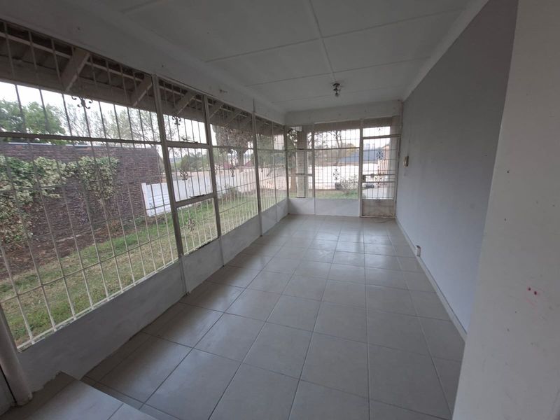 A spacious, enclosed patio area featuring tiled flooring and extensive security-barred windows, offering a bright and versatile space overlooking the garden.