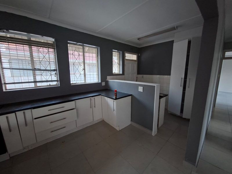 A functional kitchen featuring white built-in cabinetry, dark countertops, tiled flooring, and security bars on the windows.