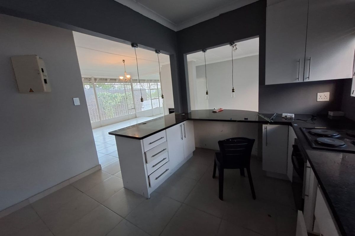 A functional kitchen featuring white cabinetry, dark stone countertops, and an electric hob, with an open-plan layout connecting to the adjacent living area.