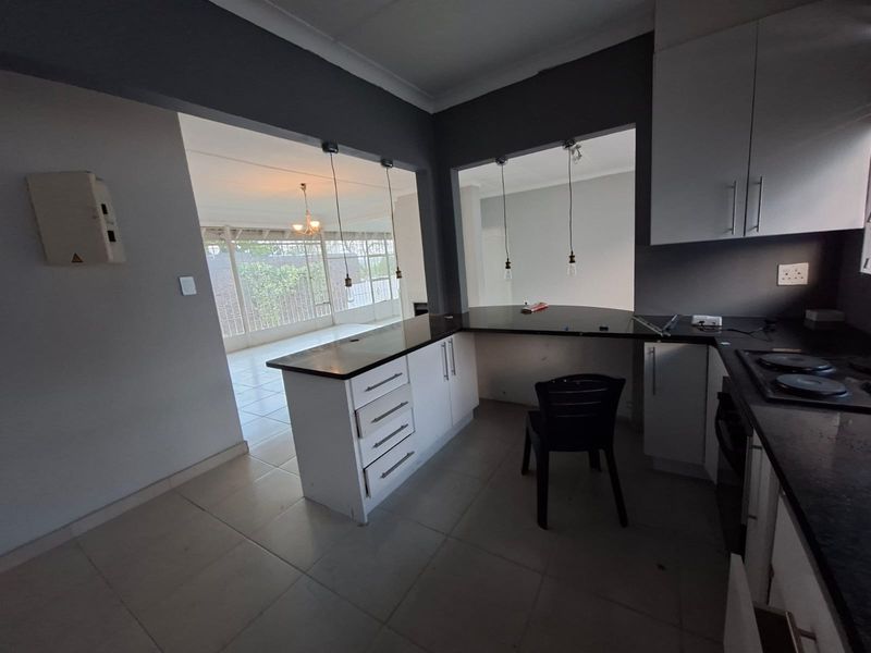 A functional kitchen featuring white cabinetry, dark stone countertops, and an electric hob, with an open-plan layout connecting to the adjacent living area.