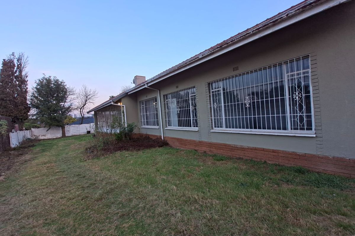 Rear view of the house featuring a large lawn, brick plinth detailing, and windows fitted with security bars.