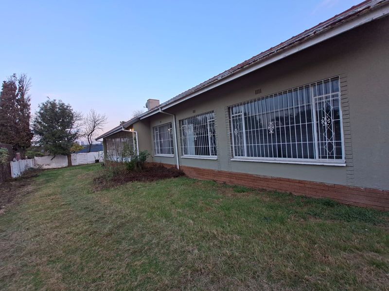 Rear view of the house featuring a large lawn, brick plinth detailing, and windows fitted with security bars.