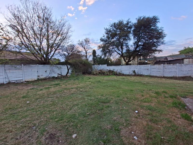 A spacious backyard area featuring a lawn and perimeter precast concrete boundary wall, requiring landscaping and maintenance to improve its overall appeal.