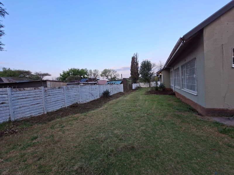 A view of the rear garden featuring a lawn area, precast concrete boundary wall, and the side elevation of the house with security-barred windows.