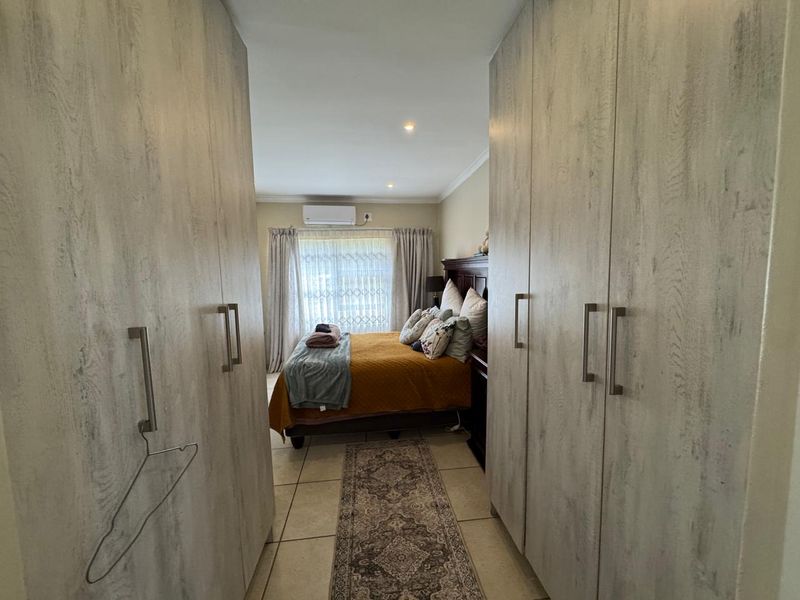 A bedroom featuring extensive built-in cupboards, tiled flooring, and a wall-mounted air conditioning unit, providing a functional and organized living space.
