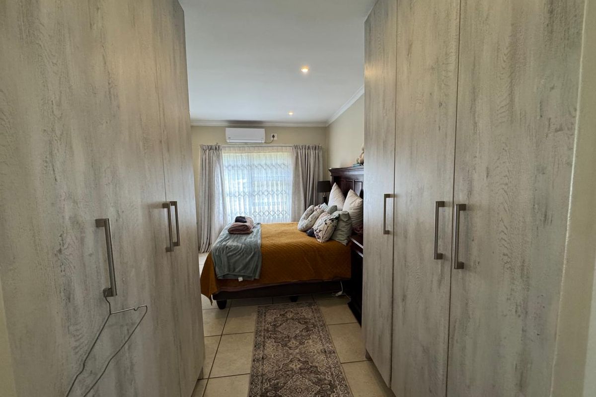 A bedroom featuring extensive built-in cupboards, tiled flooring, and a wall-mounted air conditioning unit, providing a functional and organized living space.