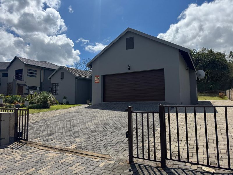 Front view of the property featuring a paved driveway, secure metal gate, and a single garage with a tiled roof.