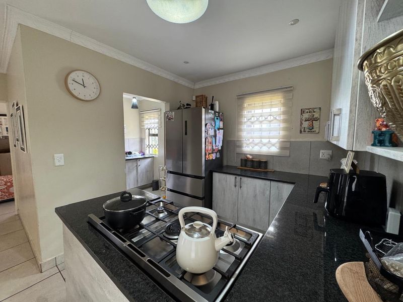 A functional kitchen featuring dark granite countertops, built-in cabinetry, and a gas hob, with an adjacent scullery area visible through the doorway.
