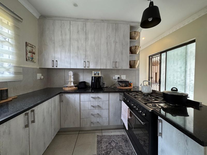 A well-maintained kitchen featuring light wood-grain cabinetry, dark granite countertops, and a built-in gas stove with oven, leading to an outdoor area.