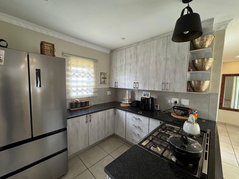 A functional kitchen featuring light wood-grain cabinetry, dark granite countertops, a gas hob, and tiled flooring, offering a clean and well-maintained workspace.