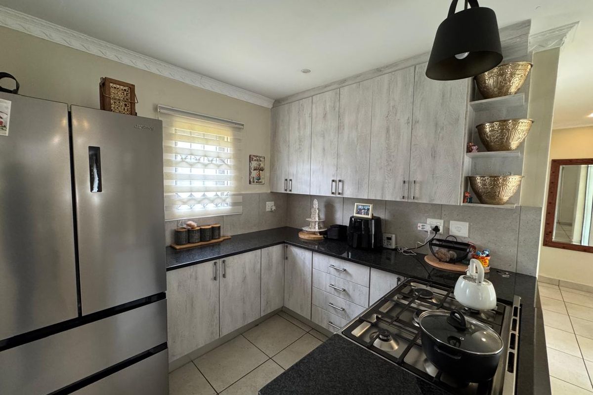 A functional kitchen featuring light wood-grain cabinetry, dark granite countertops, a gas hob, and tiled flooring, offering a clean and well-maintained workspace.