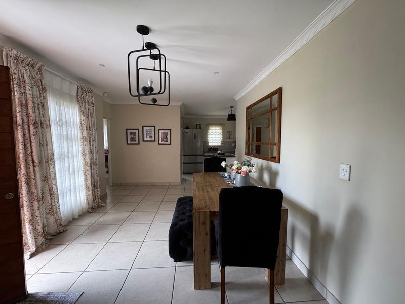 Open plan dining area featuring tiled flooring, crown molding, and modern pendant lighting, flowing into a kitchen space.