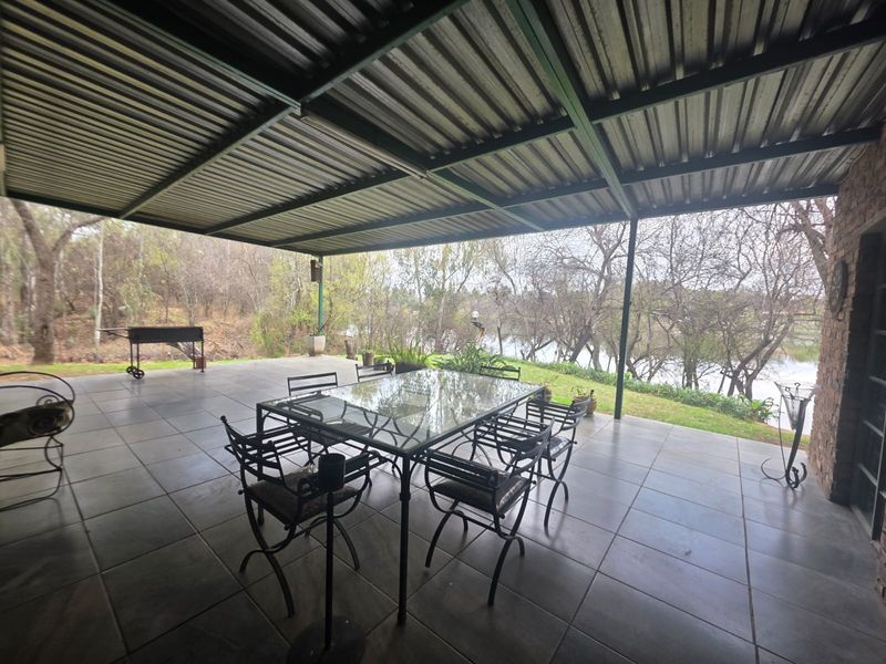 Spacious covered patio featuring tiled flooring, a corrugated metal roof, and scenic views of the surrounding trees and water.