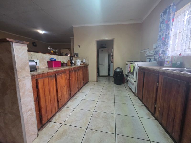 A functional kitchen featuring wooden cabinetry, tiled flooring, and a freestanding stove, offering a dated aesthetic with potential for modern renovation.