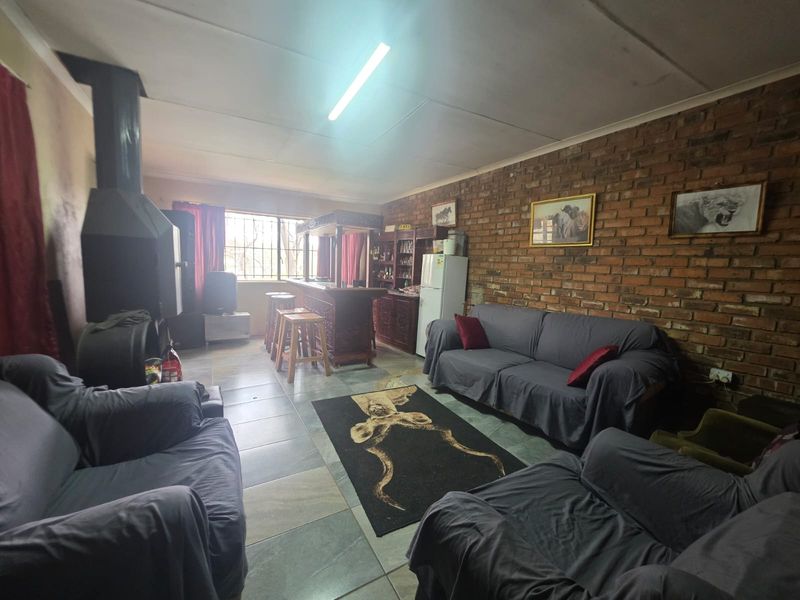 Spacious living area featuring an exposed brick wall, tiled flooring, and a prominent freestanding fireplace, offering a rustic aesthetic with potential for modernization.