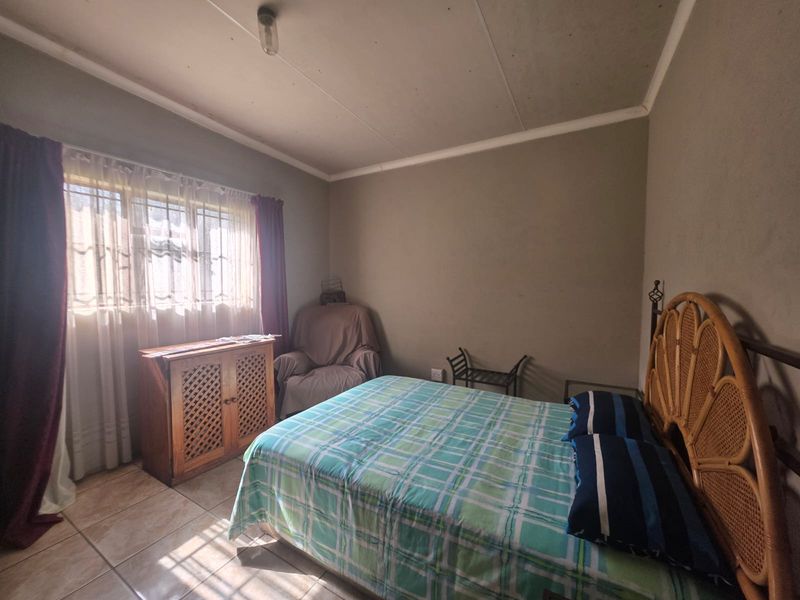 A bedroom featuring tiled flooring, a window with security bars, and a ceiling light fixture. The room requires cosmetic updates to improve its overall condition.