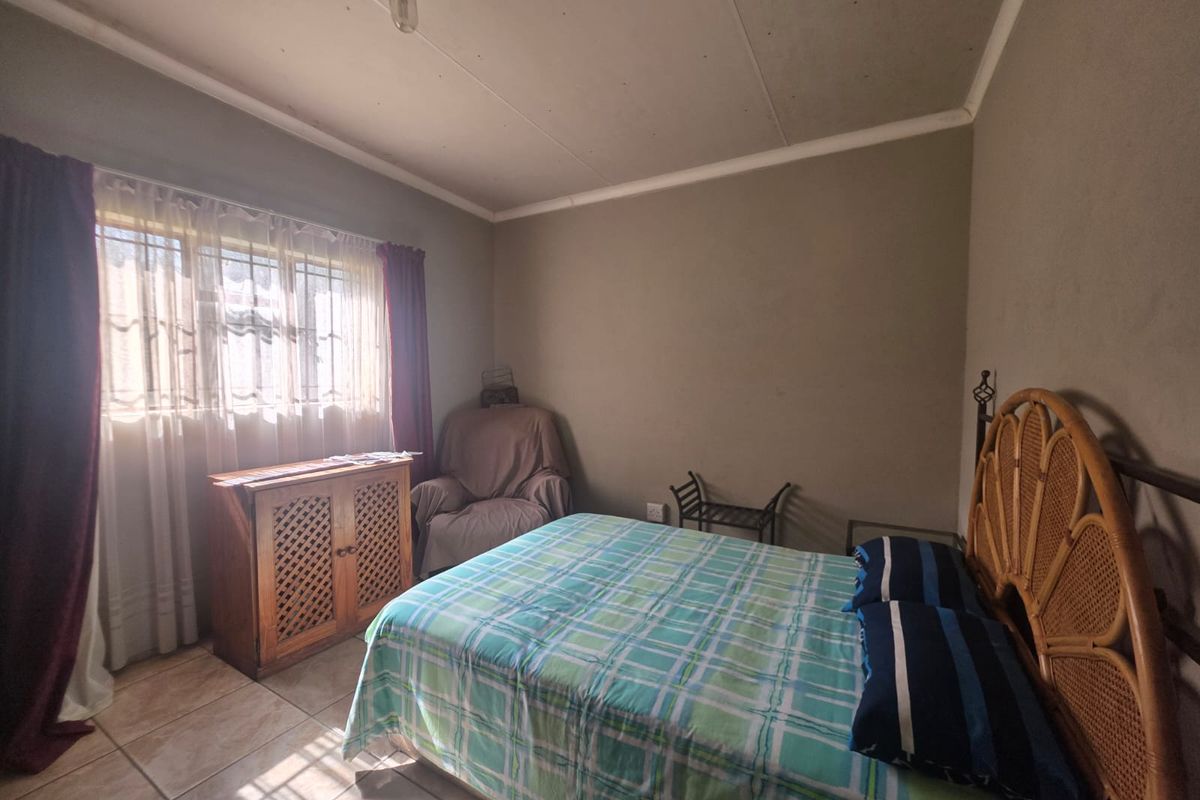 A bedroom featuring tiled flooring, a window with security bars, and a ceiling light fixture. The room requires cosmetic updates to improve its overall condition.