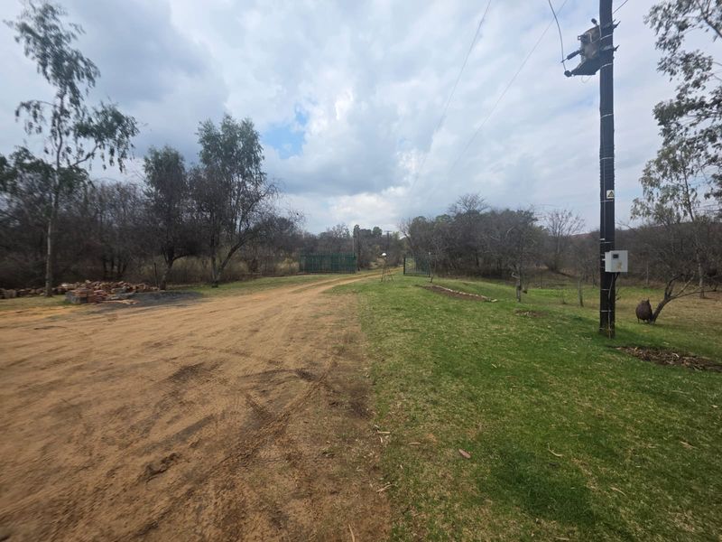 A view of the property entrance featuring a dirt driveway, green lawn, and metal security gate.
