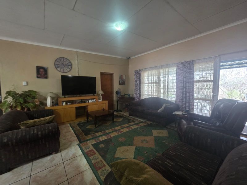 A spacious living room featuring tiled flooring, ceiling tiles, and access to an outdoor area through a sliding door with security gate.