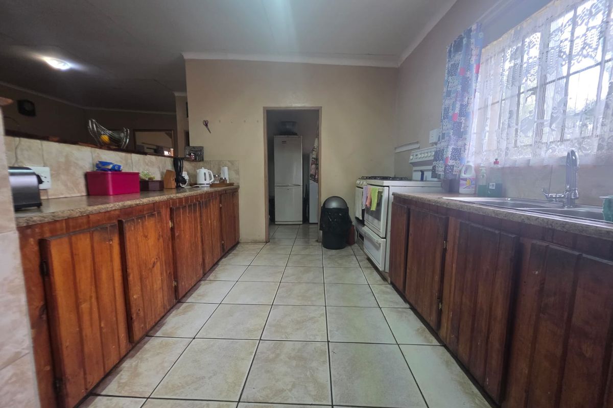 A functional kitchen featuring wooden cabinetry, laminate countertops, a double basin sink, and a freestanding stove, with tiled flooring throughout.
