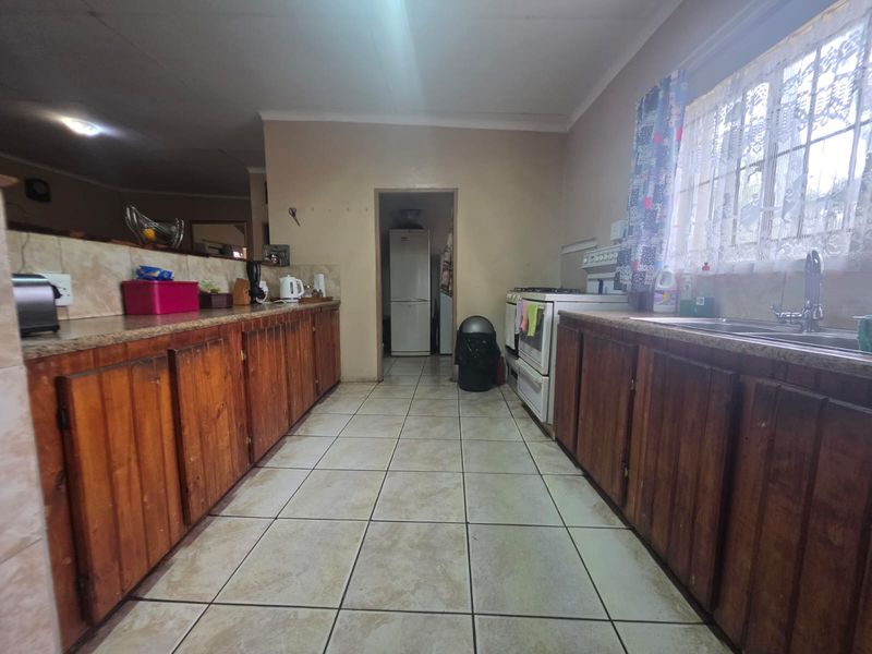A functional kitchen featuring wooden cabinetry, laminate countertops, a double basin sink, and a freestanding stove, with tiled flooring throughout.