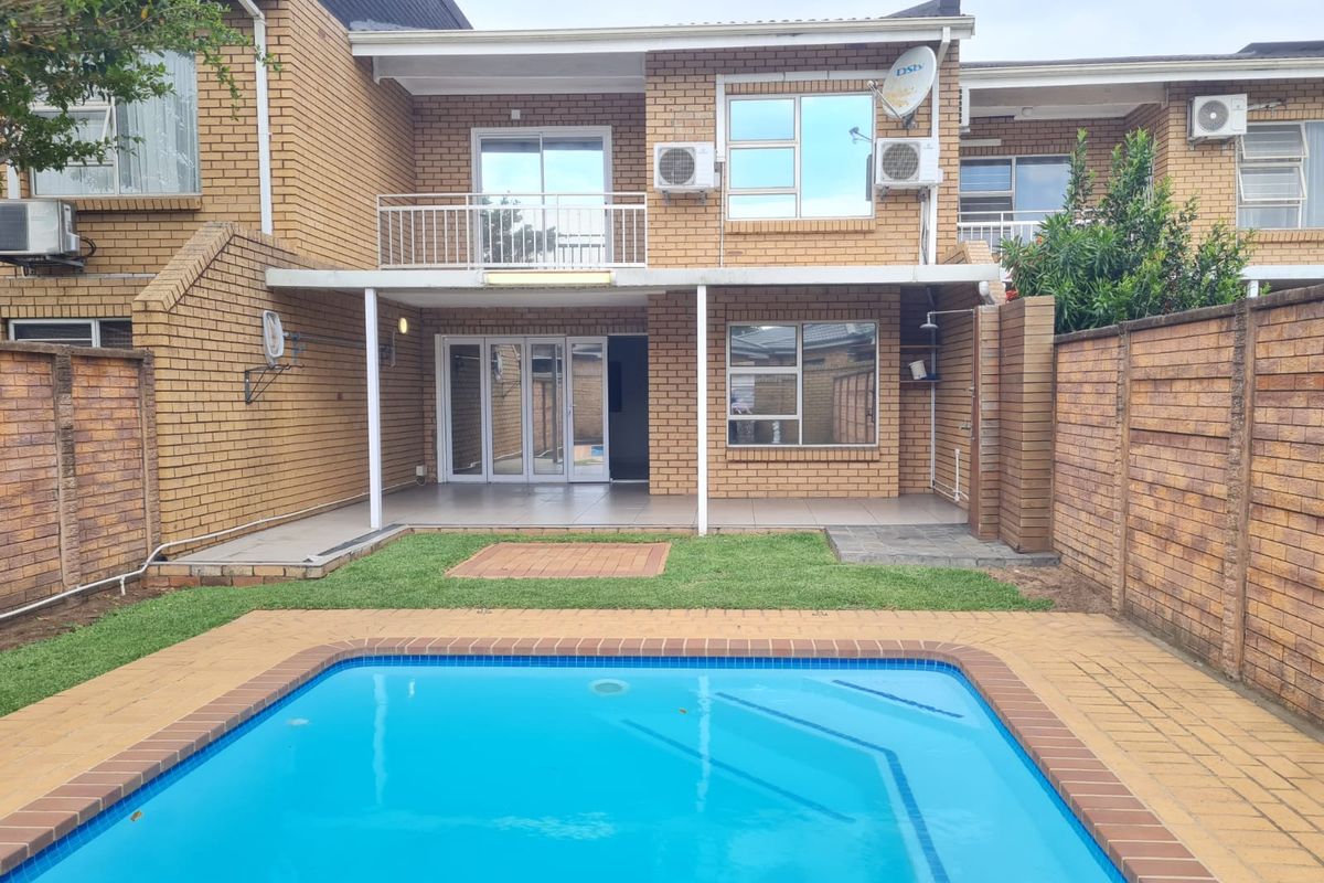 Rear view of a townhouse featuring a private swimming pool, paved patio area, balcony, and brick exterior finish.