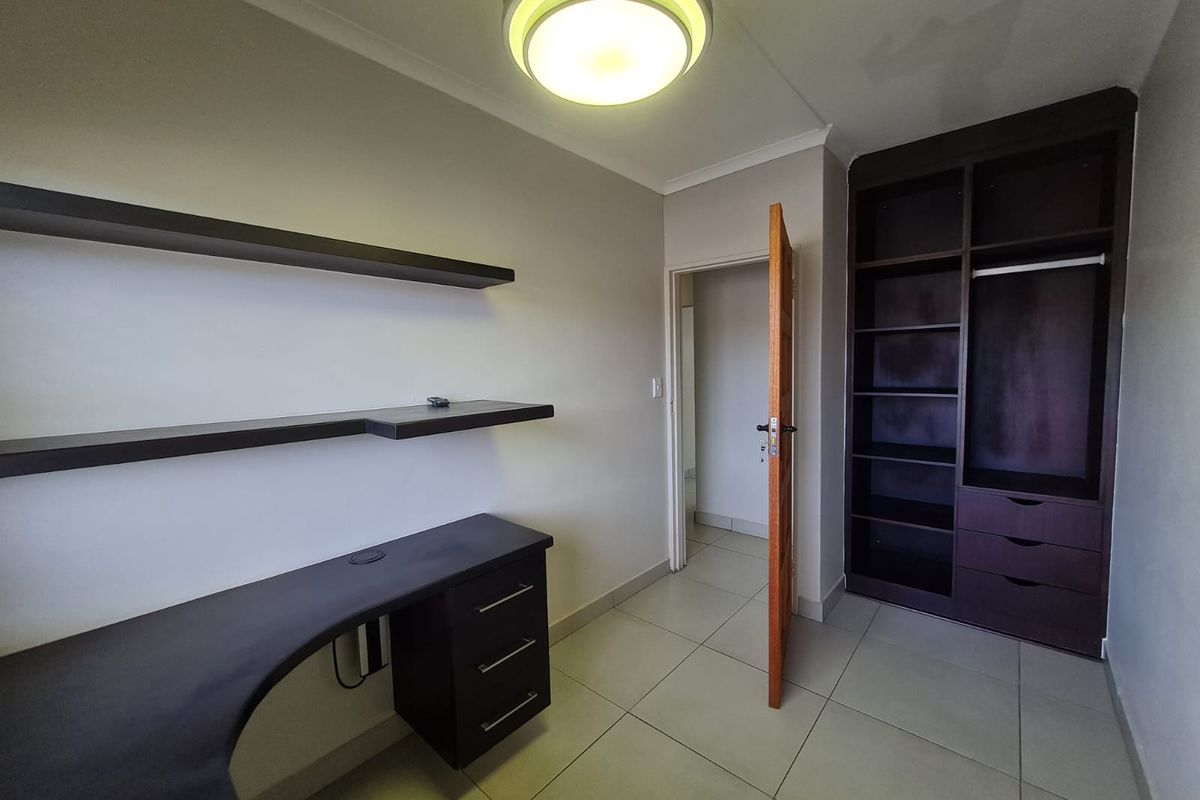 A clean, empty bedroom featuring tiled flooring, a built-in desk with floating shelves, and a spacious built-in wardrobe.