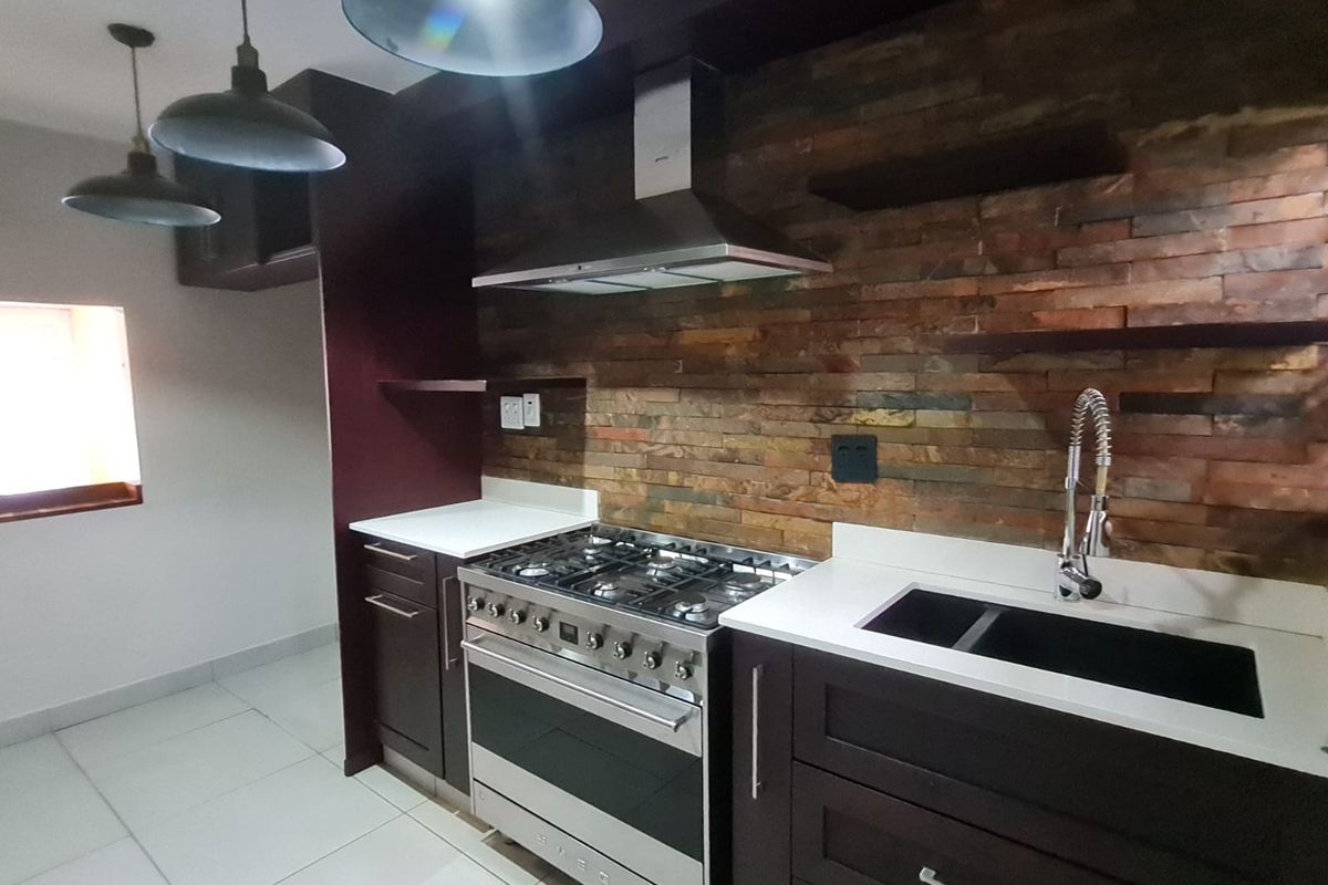 Modern kitchen featuring dark cabinetry, stone countertops, a gas stove with extractor fan, and a distinctive stone-clad backsplash.