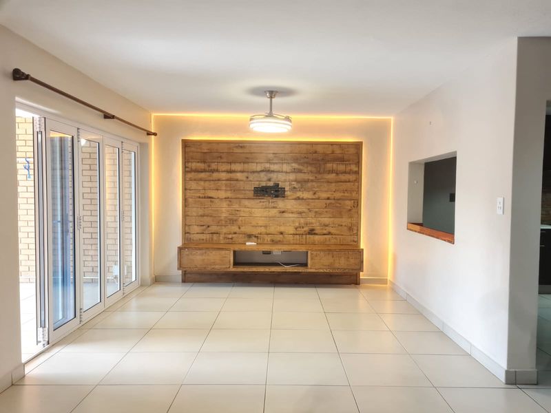 Spacious living room featuring a custom built-in wooden media unit with ambient LED lighting, tiled floors, and folding glass doors leading to the exterior.
