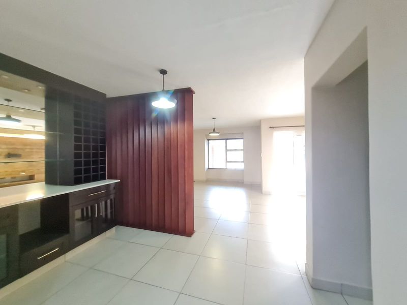 Spacious open-plan living area featuring neutral tiled flooring, a built-in wine rack, and a decorative timber slat room divider.