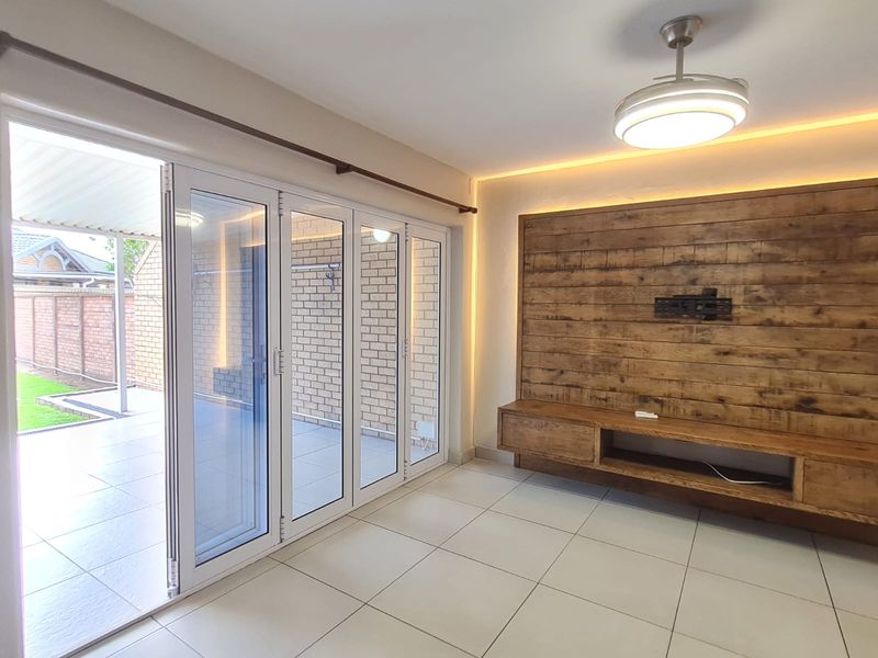 Modern living room featuring large bi-fold glass doors opening to a patio, a wood-paneled feature wall with built-in media console, and recessed ambient lighting.