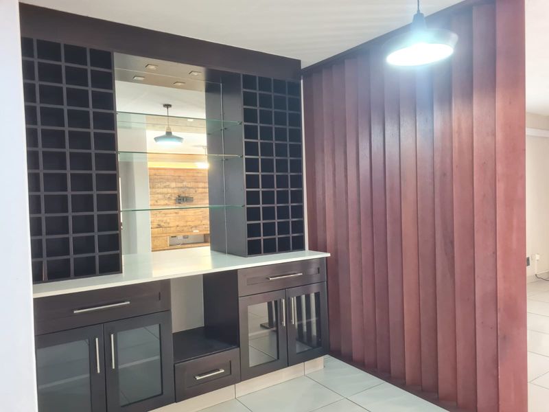 A dedicated bar area featuring custom built-in cabinetry with integrated wine storage, glass shelving, a mirrored backsplash, and decorative vertical timber wall paneling.