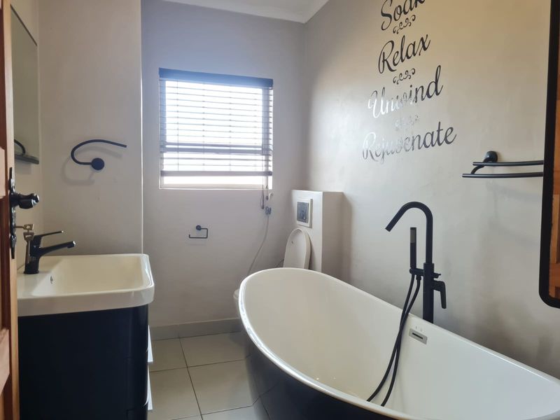 Modern bathroom featuring a sleek freestanding bathtub, wall-mounted matte black fixtures, a vanity basin, and a concealed cistern toilet with neutral tiling.