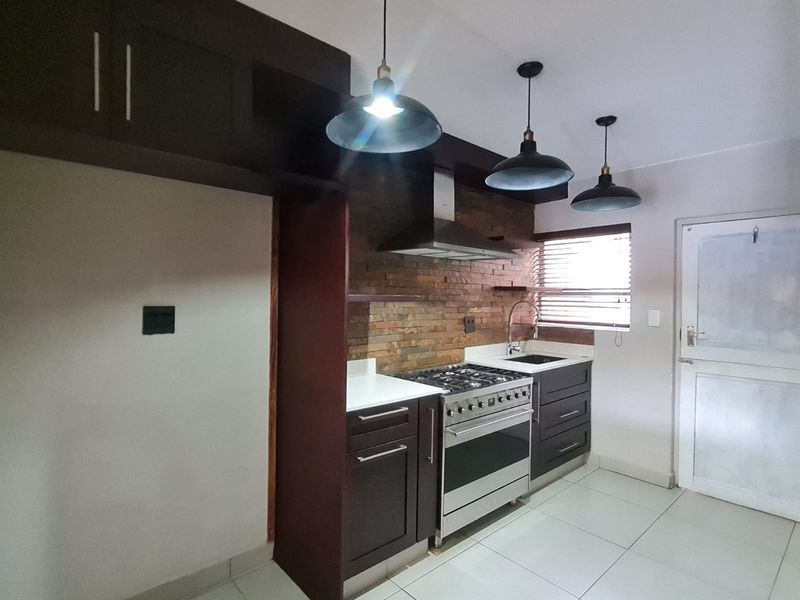Modern kitchen featuring dark cabinetry, a gas stove with extractor fan, stone tile backsplash, and tiled flooring, offering a clean and functional workspace.