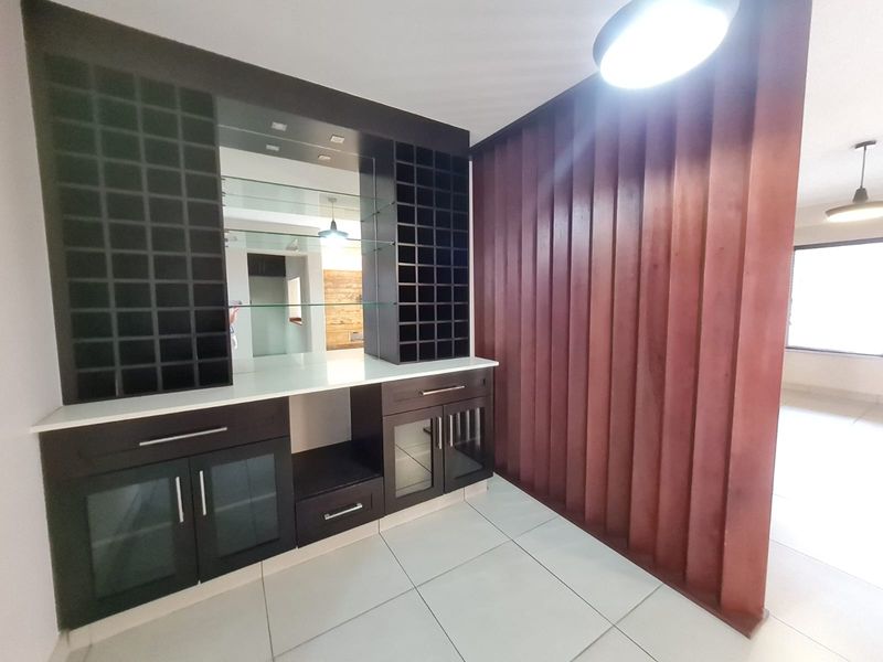 A dedicated bar area featuring custom built-in cabinetry with wine storage, glass shelving, a mirrored backsplash, and a decorative vertical timber slat feature wall.