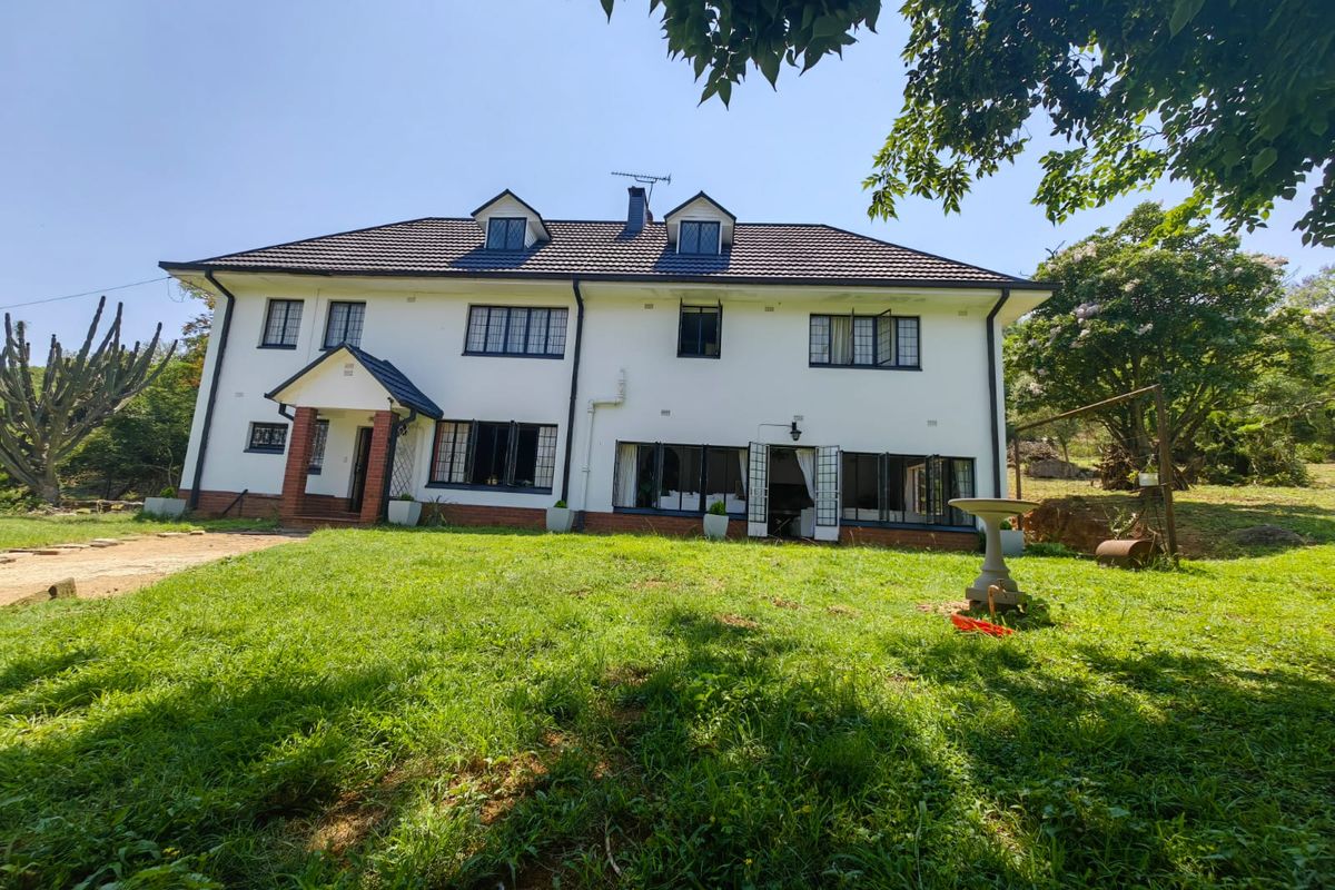 A rear view of a two-story residential house featuring a tiled roof, dormer windows, and a large garden area.