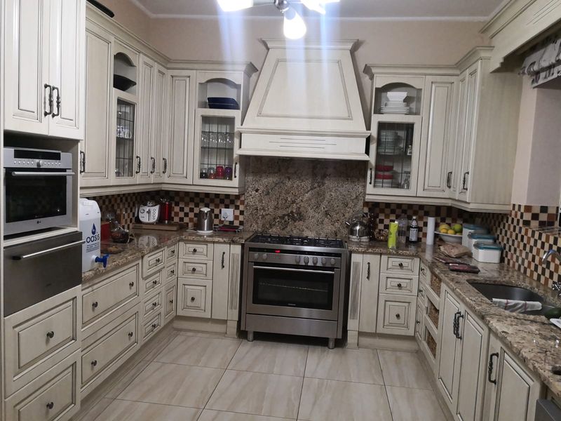 A traditional kitchen featuring cream-colored cabinetry, granite countertops, a gas stove with a decorative extractor hood, and tiled flooring.