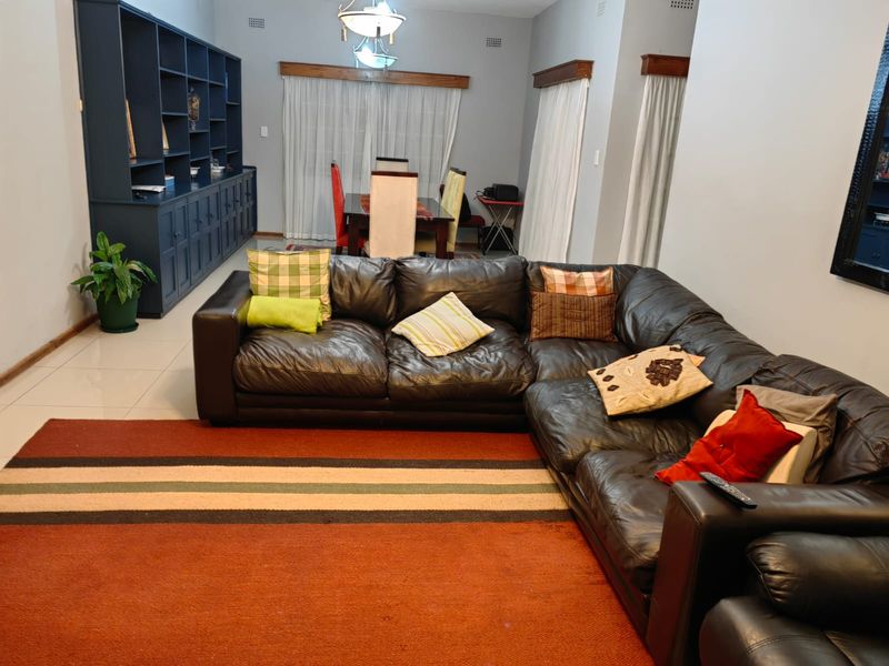 Spacious open-plan living and dining area featuring tiled flooring, built-in cabinetry, and large windows with curtain rails.