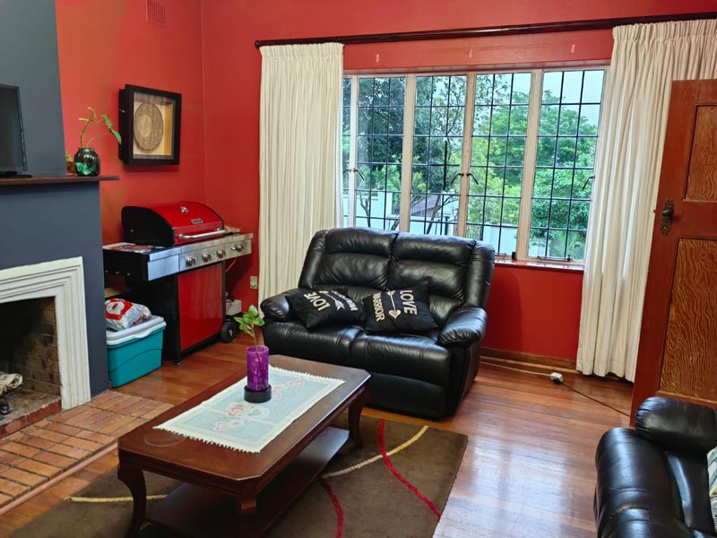 Living room featuring a brick fireplace, timber flooring, and large leaded glass windows overlooking the garden.