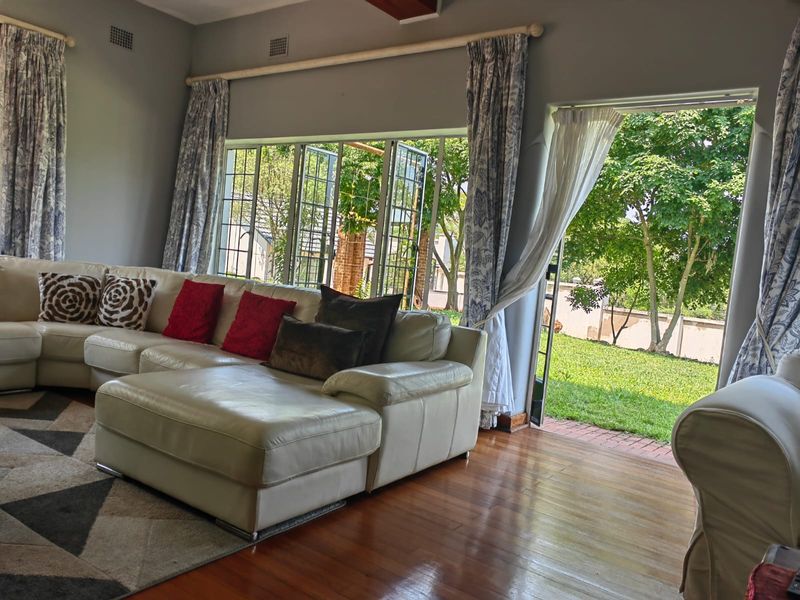 A bright living room featuring polished hardwood floors, large steel-framed windows, and direct access to the garden through glass-paned french doors.