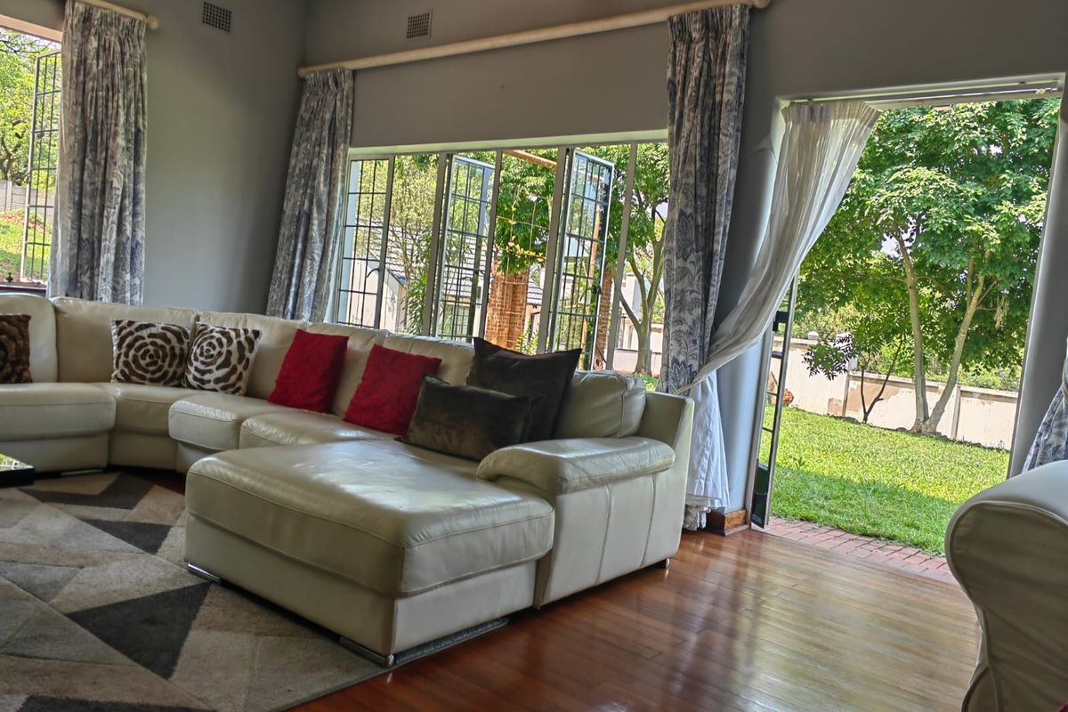 Spacious living room featuring polished hardwood floors, large steel-framed windows, and direct access to the garden through a glass door.