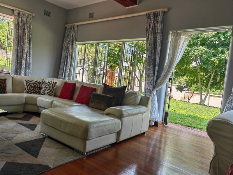 Spacious living room featuring polished hardwood floors, large steel-framed windows, and direct access to the garden through a glass door.