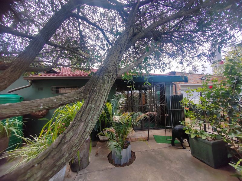 Rear exterior view of the property featuring a paved patio area, security gate access, and a water tank, shaded by mature trees.