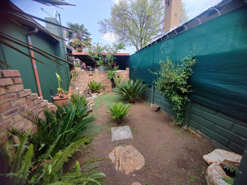 A private rear garden area featuring brick boundary walls, privacy screening, and established landscaping with paved stepping stones.