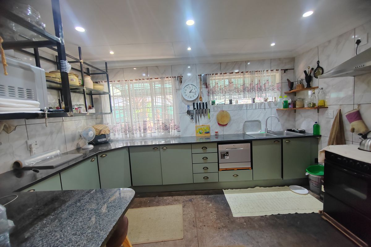 A functional kitchen featuring granite countertops, ample built-in cabinetry, a stainless steel sink, and a tiled backsplash with integrated extractor fan.