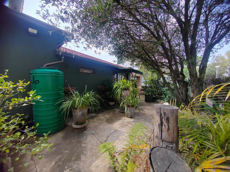 A rear exterior view showing a paved area, mature trees, and a large green water tank attached to the side of the house.