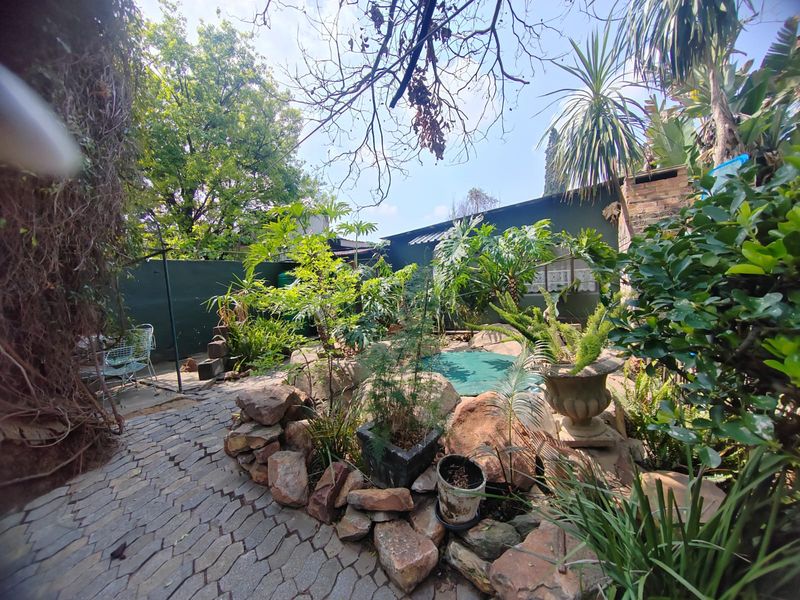 A private outdoor pool area featuring a rock-lined garden, paved pathways, and established greenery, offering a secluded backyard setting.